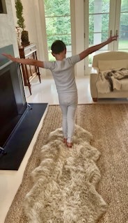 A child balancing with arms outstretched while walking along a rug in a living room.
