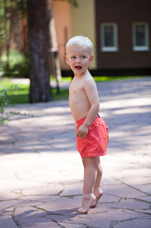 A toddler in red shorts standing barefoot on tiptoe on a stone path outdoors.
